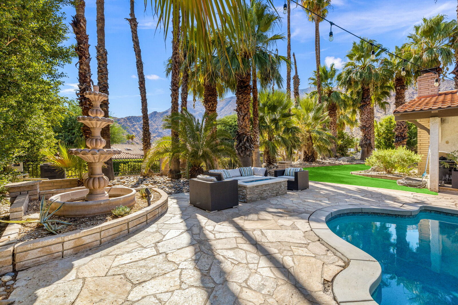 Stone patio with a tiered fountain, lounge seating, and palms around the pool