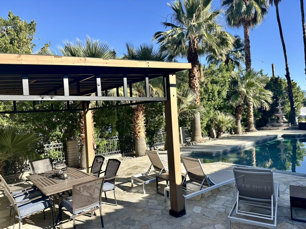 Pergola-shaded dining table and sun loungers on the stone pool deck at Villa 700, beside the pool and fountain with palms and mountain views