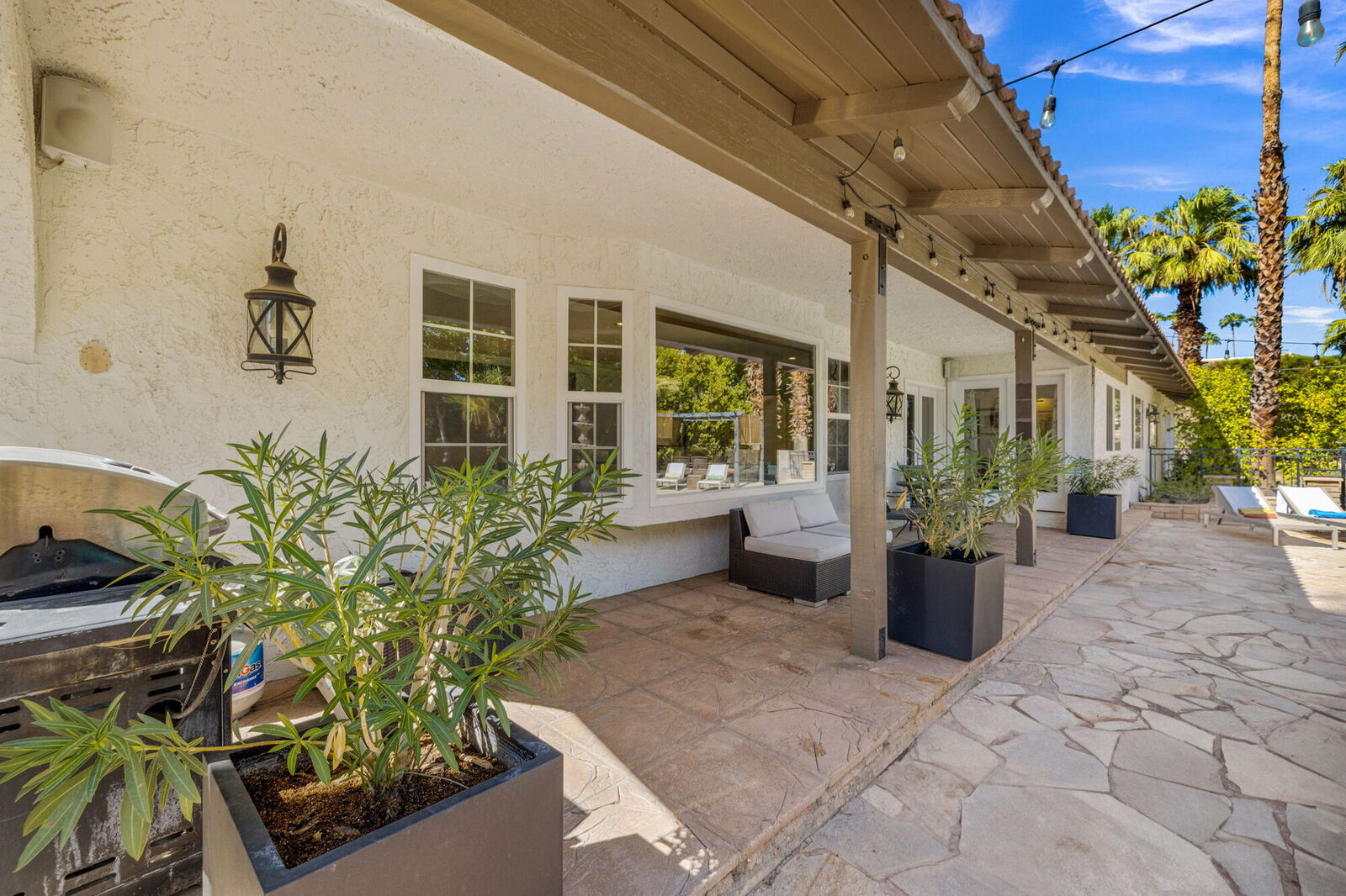 Covered patio with outdoor seating, BBQ, and string lights along the back of the house